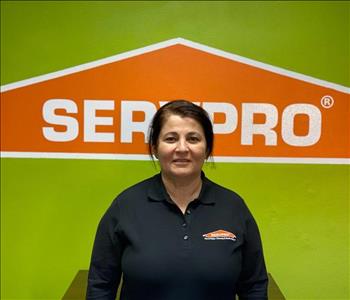 Brown haired female standing in front of a SERVPRO green background with a SERVPRO logo on the wall. 