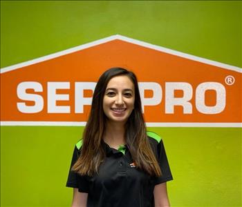 Brown haired female standing in front of a SERVPRO green background with a SERVPRO logo on the wall. 