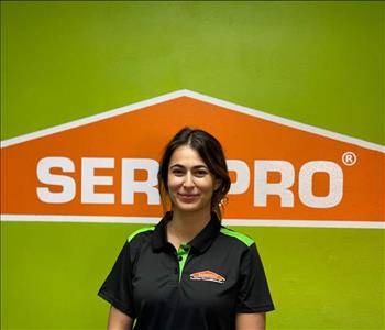 Brown haired female standing in front of a SERVPRO green background with a SERVPRO logo on the wall. 