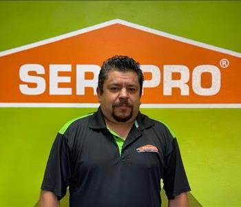 Brown haired male standing in front of a SERVPRO green background with a SERVPRO logo on the wall. 